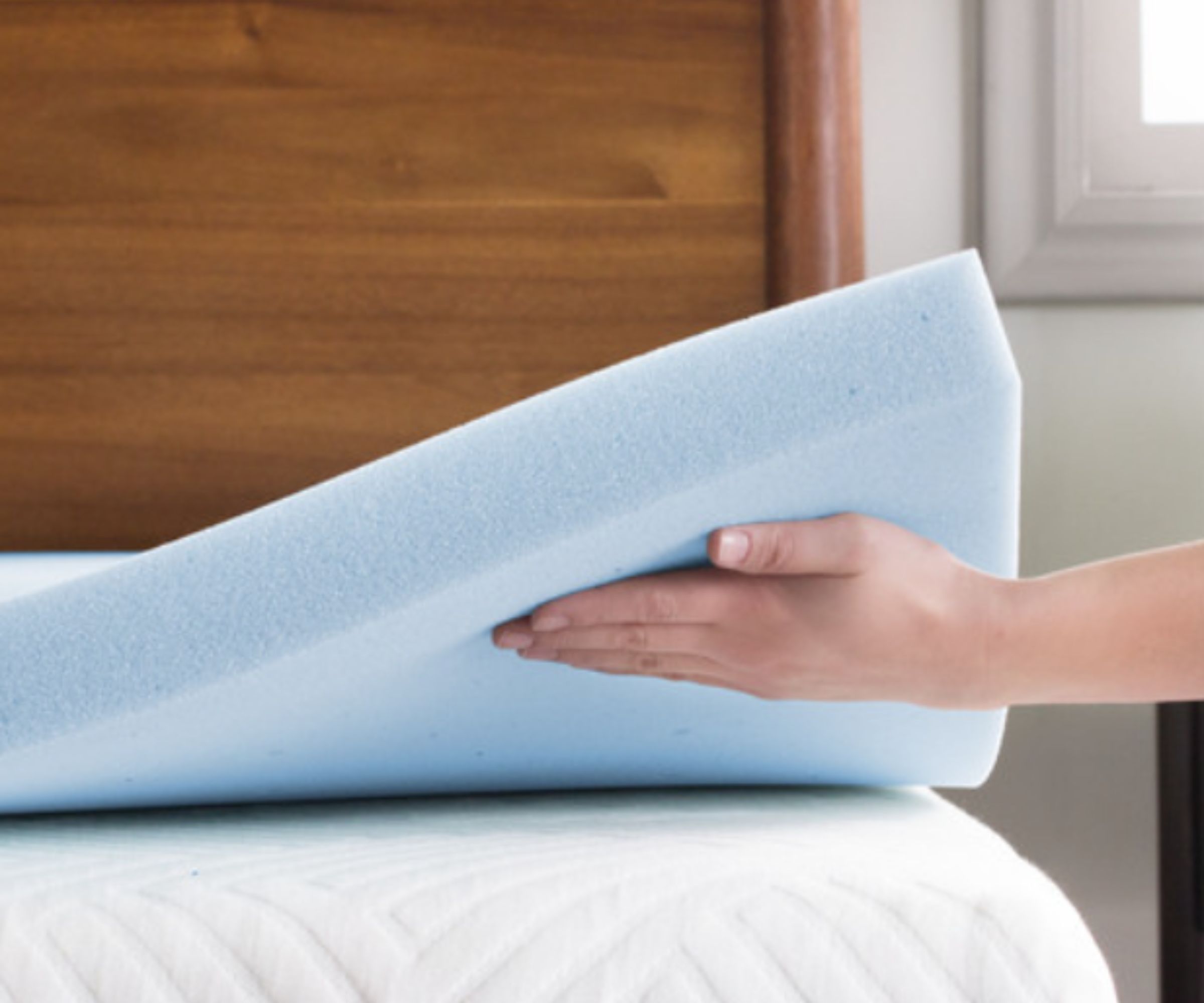 Hand holding up a Lucid mattress topper on the corner of a bed