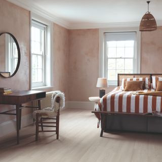 White Premium Oak laminate floor by Quick-Step in a bedroom with earthy limewashed walls and striped bedding on the bed