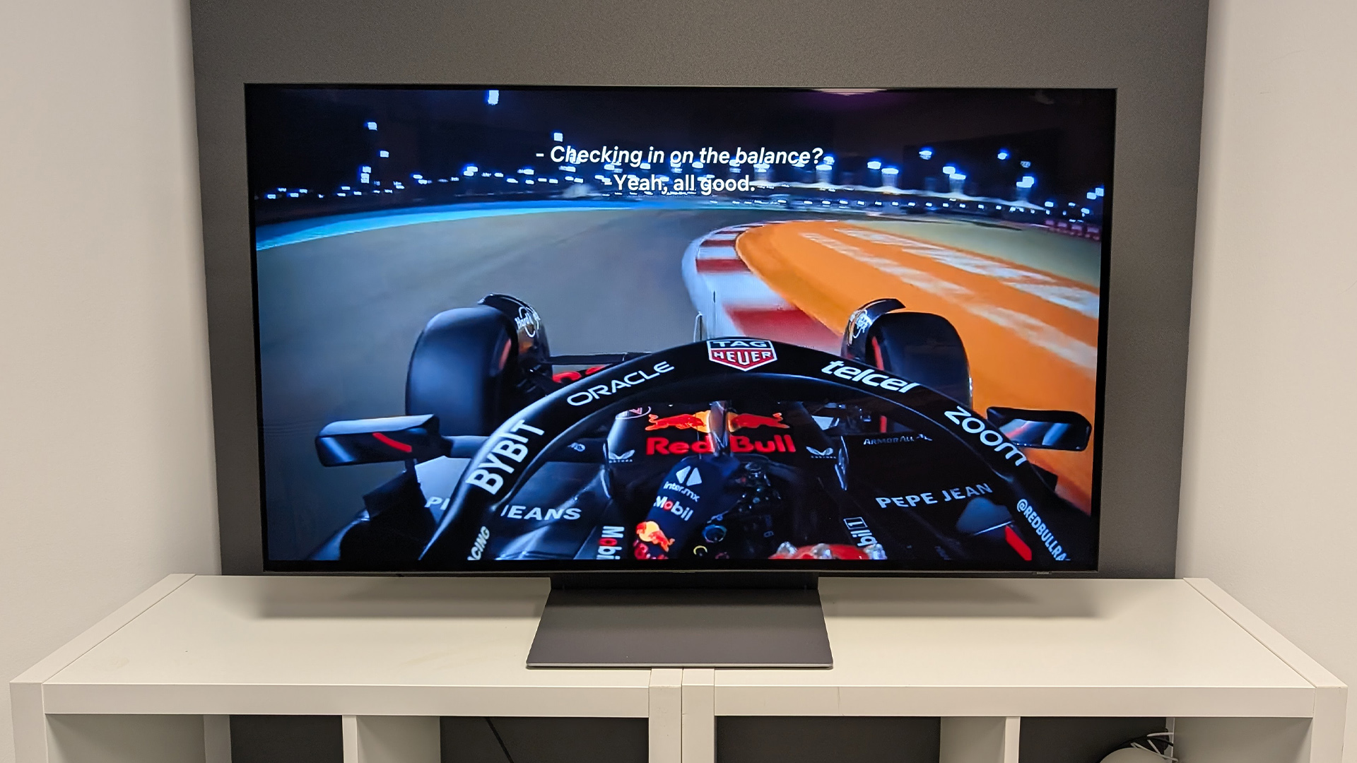 Samsung S90F 48-inch OLED TV on white wooden furniture, onscreen is cockpit view of F1 racetrack