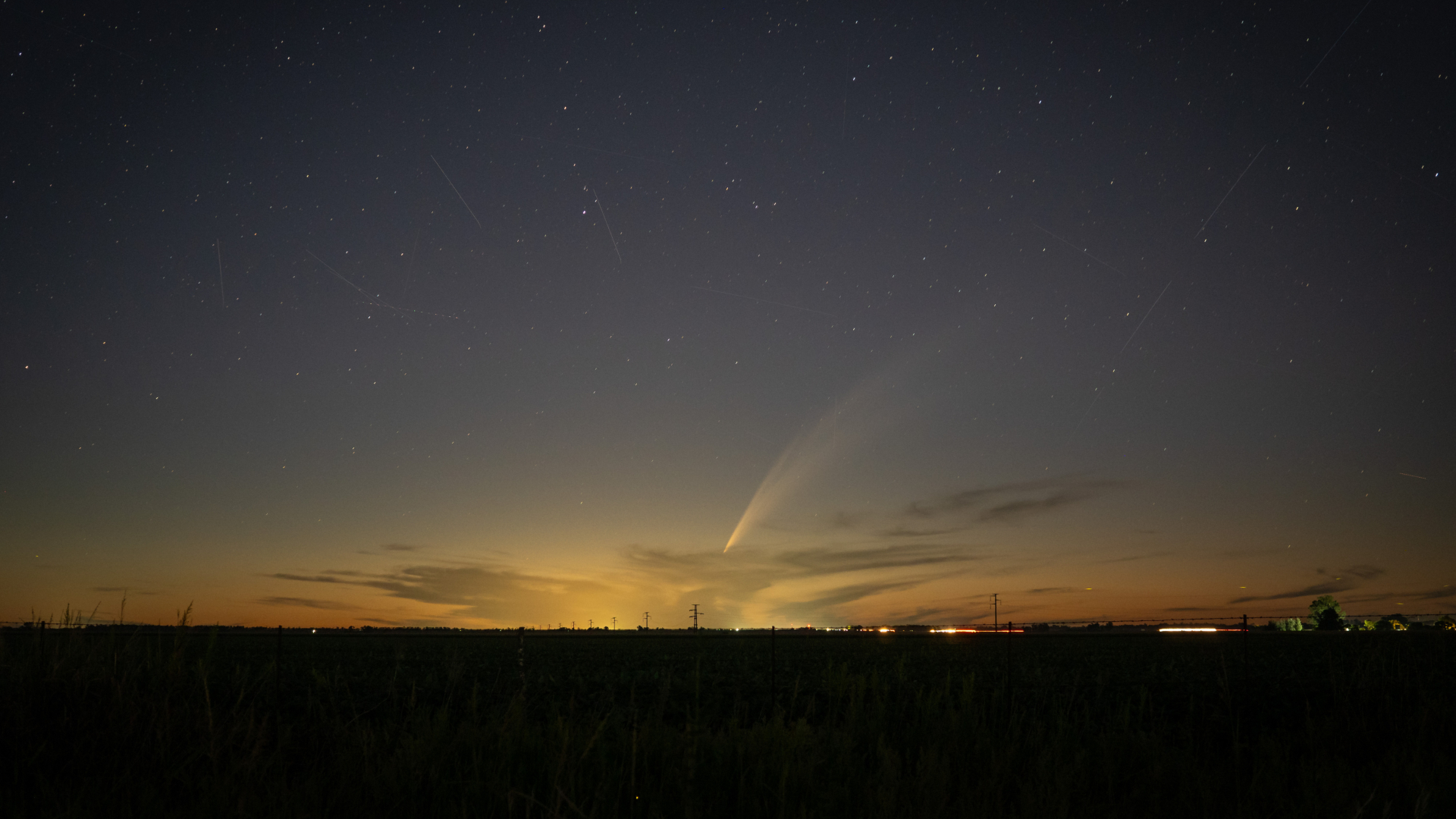 A streak of white light is seen in a sunset which is Comet G3 ATLAS with a silhouette of the landscape in the foreground