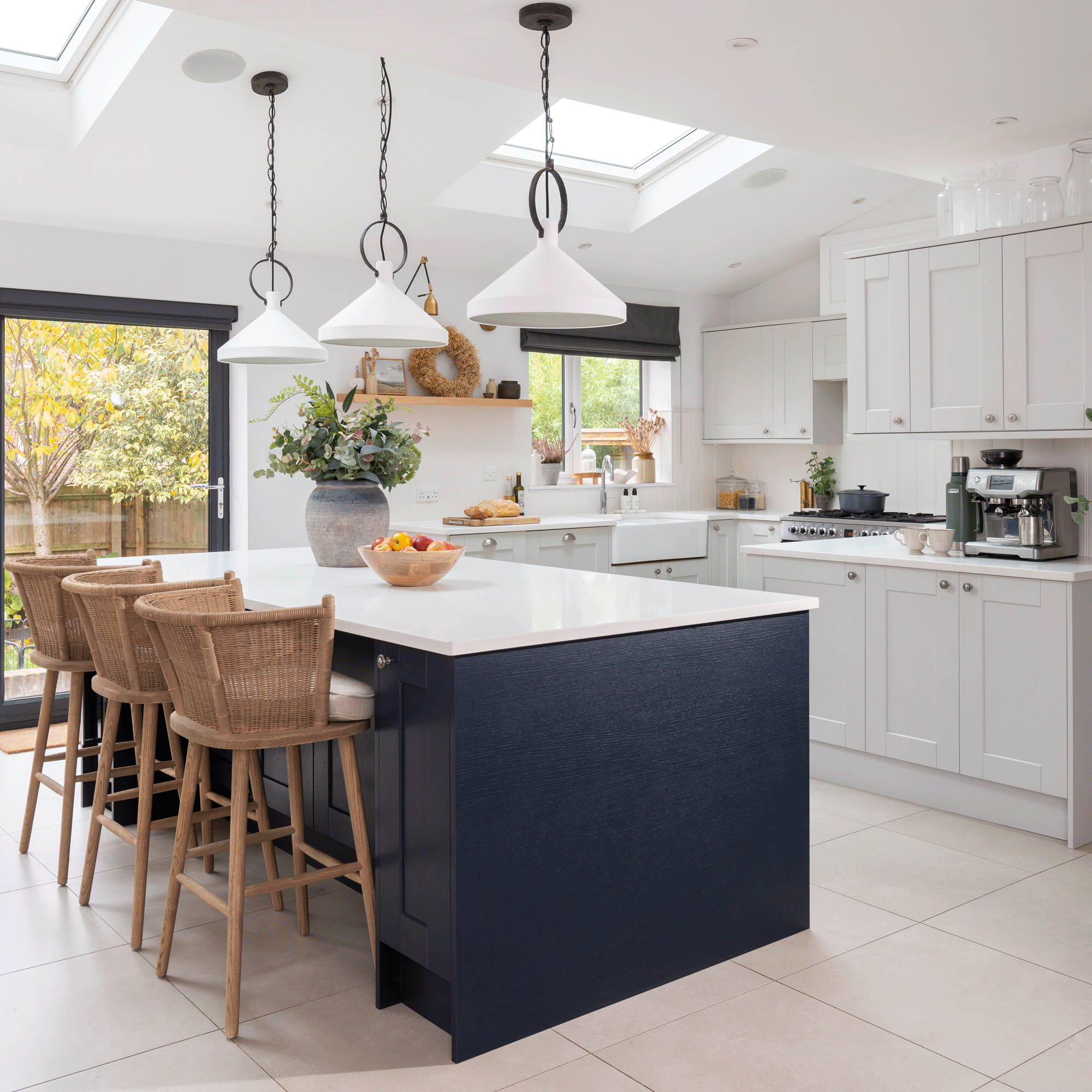 a white shaker kitchen with a black kitchen island a row of three pendant lights overhead with two skylights and a Sage coffee machine