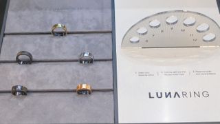 Hands-on with the Luna Ring 2 smart ring shown in five finishes in a display case next to a ring size chart showing sizes six to 12