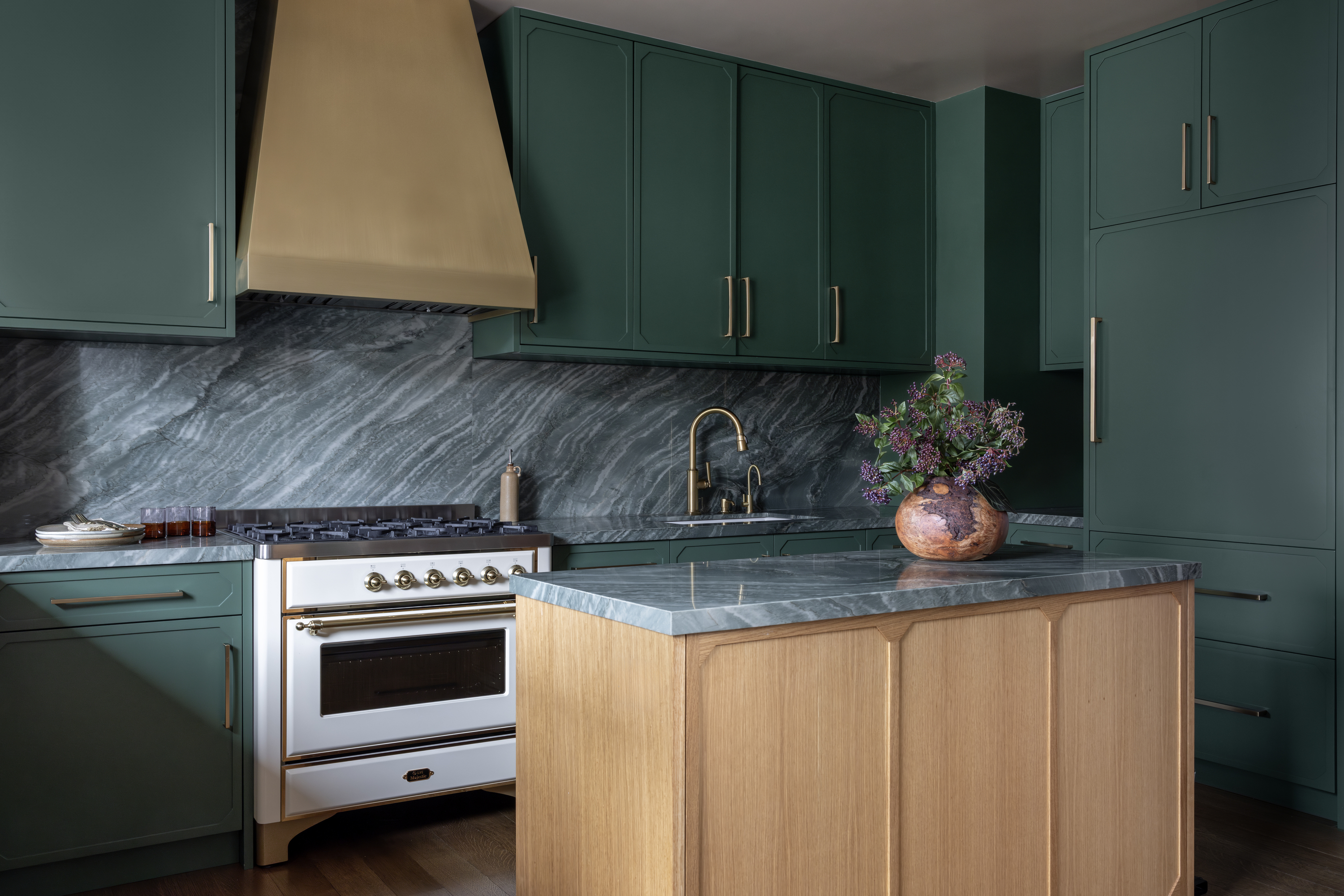 A kitchen with deep green cabinets and a wooden island