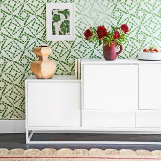 White gloss sideboard against a green patterned wallpaper wall with scallop edge rug beneath