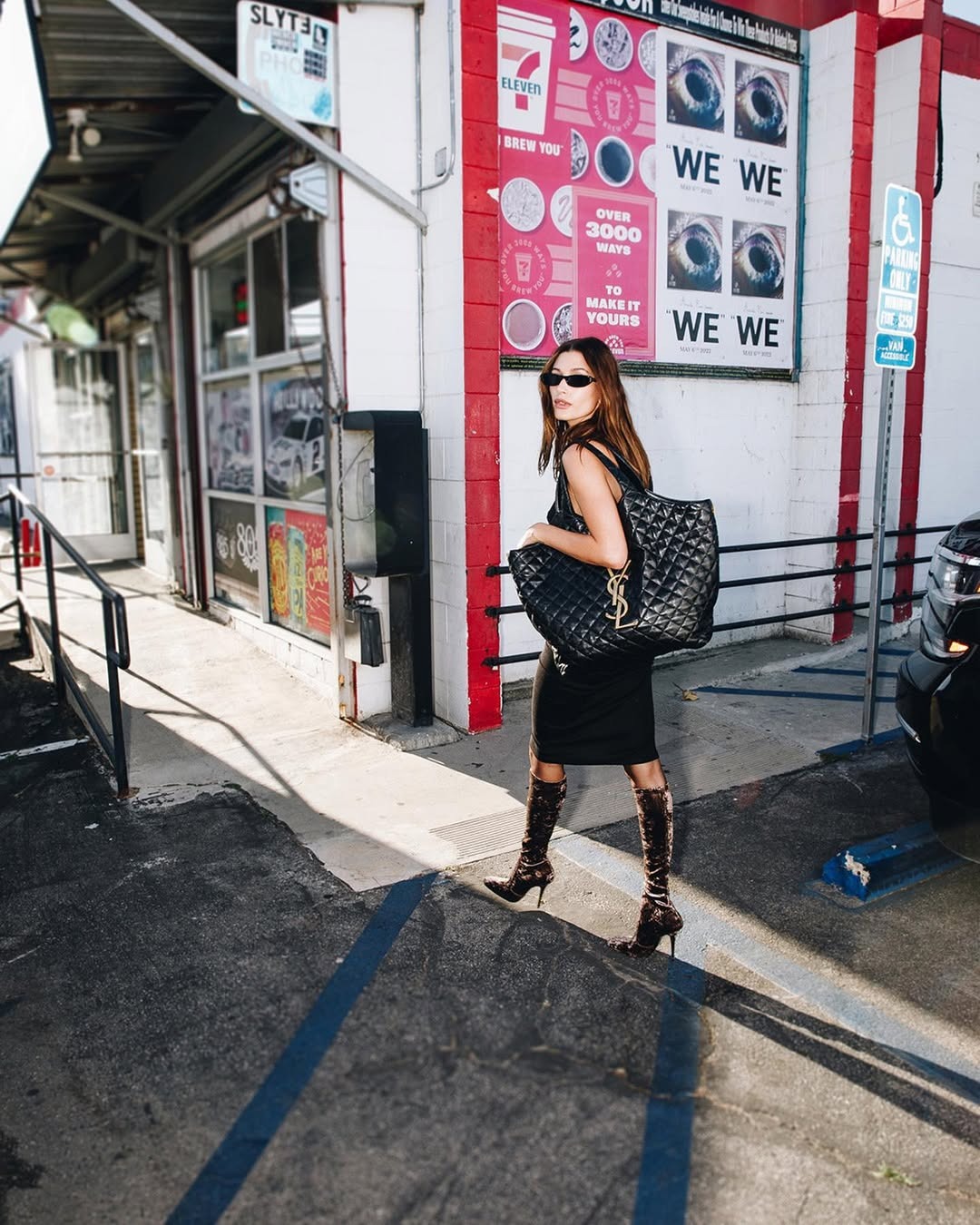Hailey Bieber wears a black dress, black knee-high boots and carries a Saint Laurent Icare tote bag