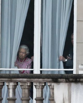 Queen Elizabeth II peeking out the windows of Buckingham Palace