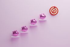 Four hot pink metallic piggy banks on their own separate steps leading up to a bullseye.