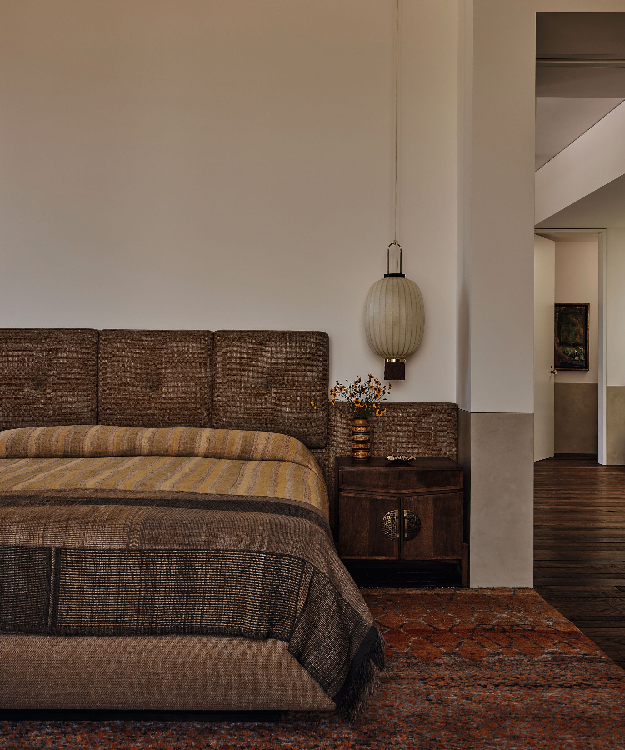 Earth-toned bedroom featuring an upholstered headboard, patterned textiles, a vintage wood nightstand, and a hanging lantern pendant.