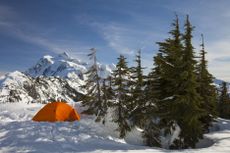 An orange tent on a snow-covered ground in front of mountains