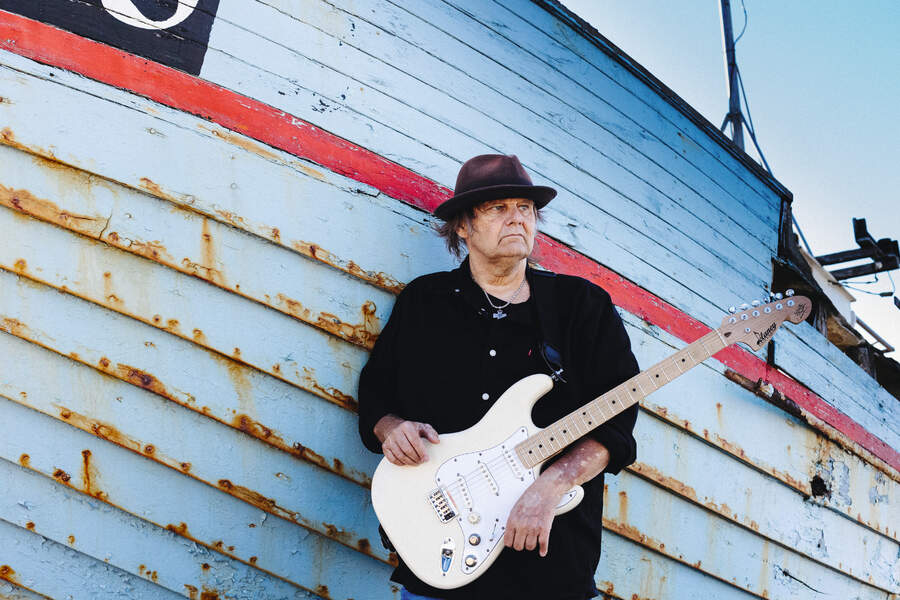 Water Trout standing in front of a fishing boat holding a guitar