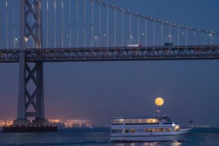 The Harvest Moon appears to perch on top of a boat beneath California's San Francisco-Oakland Bay Bridge in this photo taken by Kwong Liew on Sept. 24, 2018.