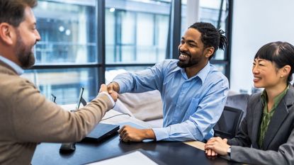 A financial planner shakes hands with a client in the adviser&#039;s office.