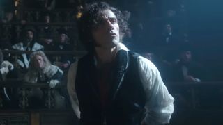 Oscar Isaac stands with a look of curiosity in a room of spectators in Frankenstein.