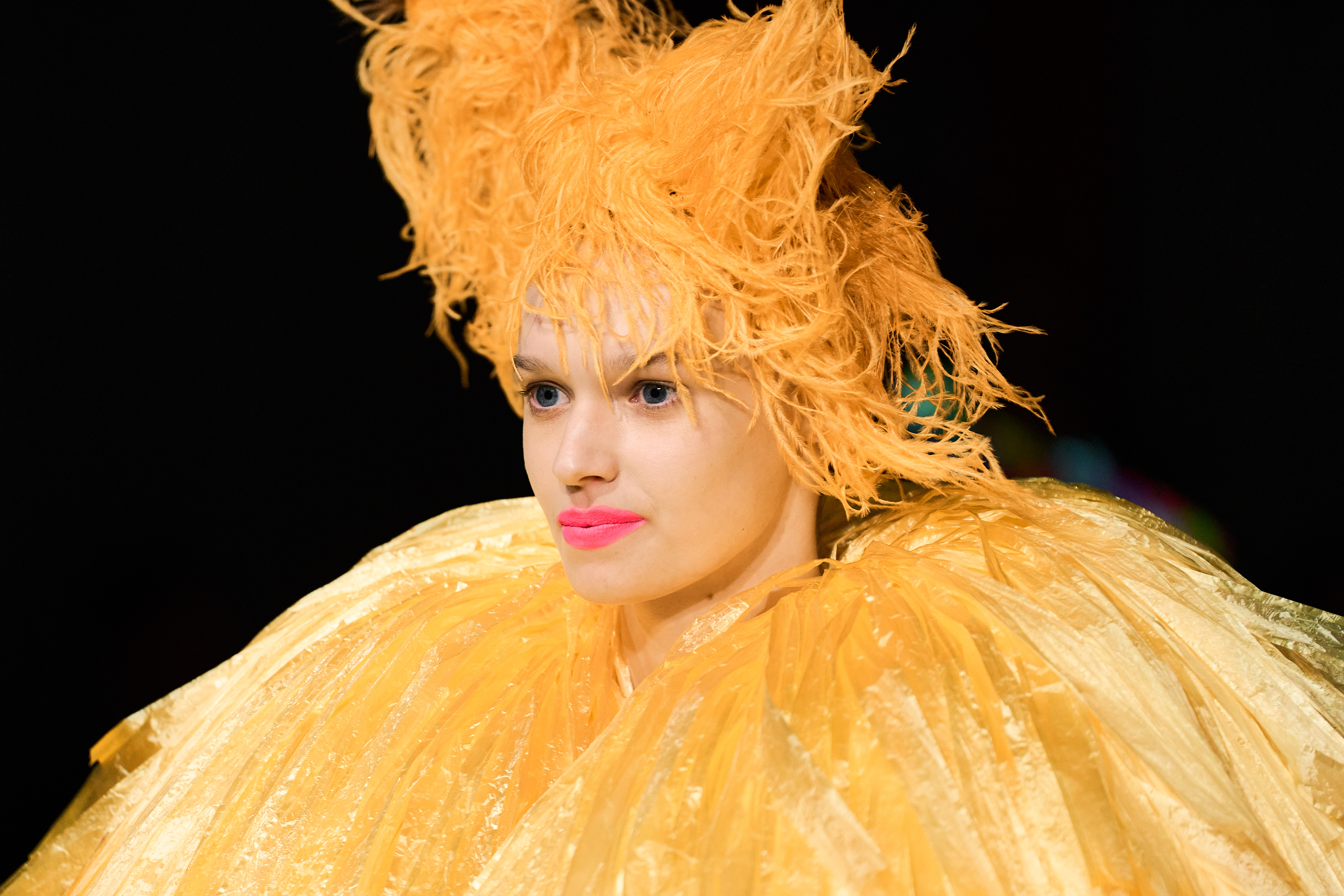 A runway model photographed wearing a bright yellow headpiece and a tulle dress