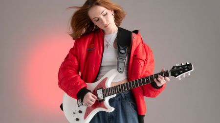A photo of a woman playing a Venus Revolution guitar in white with a red pickguard