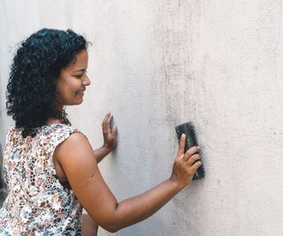 woman cleaning black marks off external wall with brush