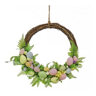 A circiular dark brown branch wreath with green leaf foliage and pastel colored eggs adorning the lower edge of it