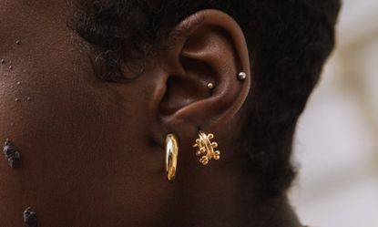 Close up of woman wearing two different gold huggie earrings and a silver bar in one ear