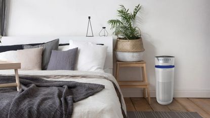 HoMedics TotalClean 5-in-1 Tower Air Purifier in white next to bedside table with plant