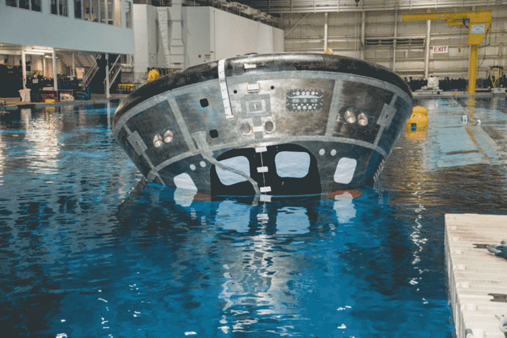 A gif showing a metal round capsule moving in a large pool with four large balloons.