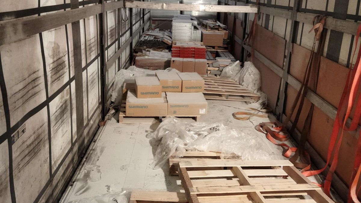 Inside the back of a lorry, mostly empty except for some empty pallets and a small pile of Shimano boxes