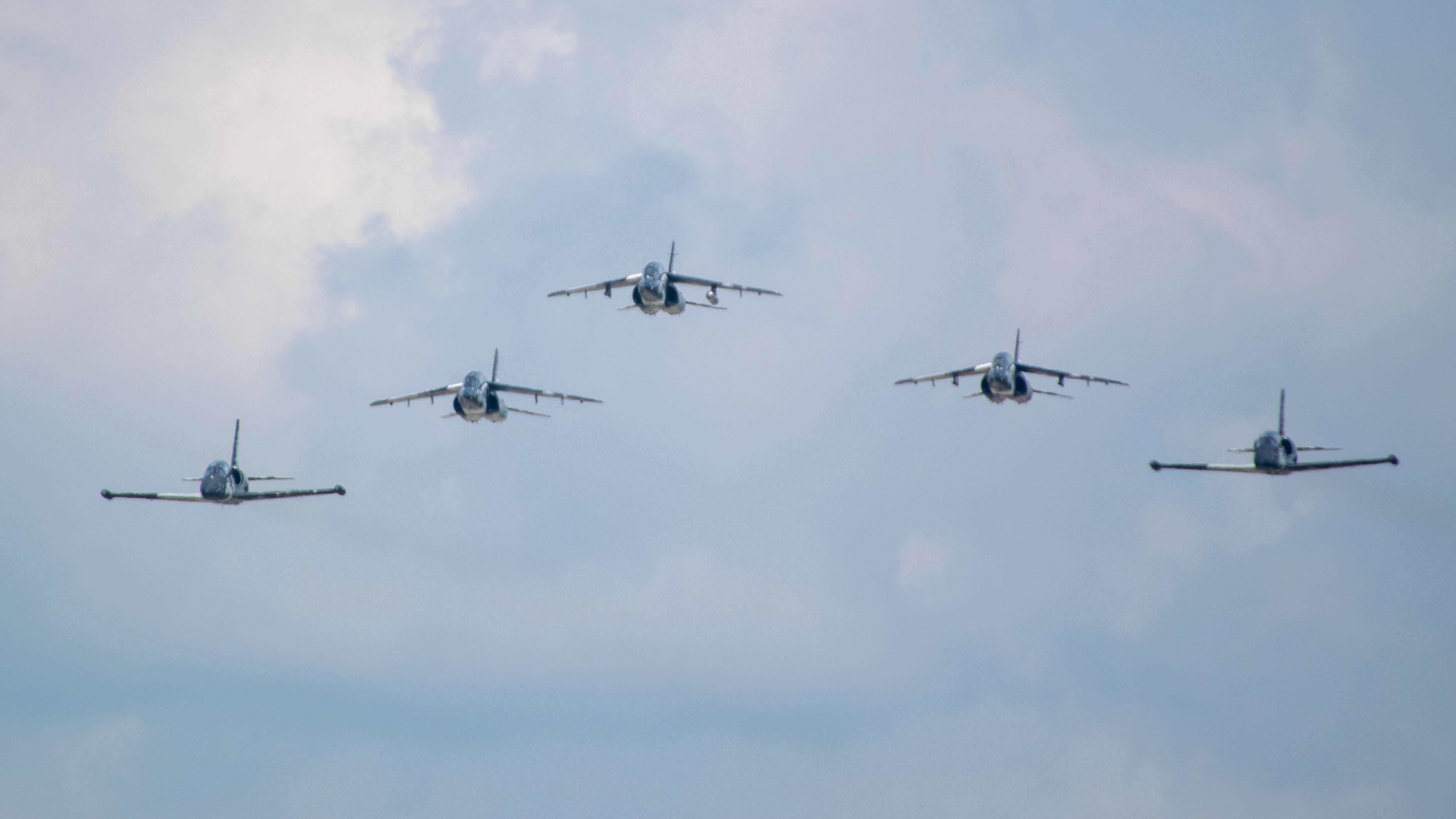 Five jets fly in formation in a blue sky.