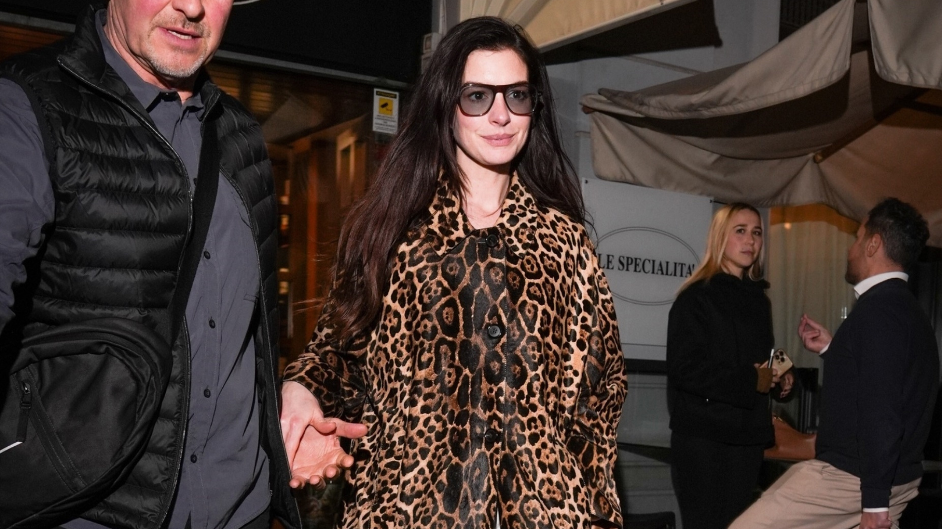 An image of Anne Hathaway wearing a leopard print coat with white jeans and clogs whilst out in Milan.