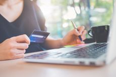 Woman holding debit card and using laptop in cafe