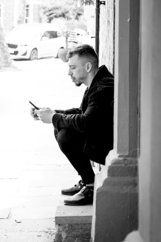 Image of a squatting man using his phone, in black-and-white, taken on the Sigma 18-50mm f/2.8 DC DN | C Canon RF