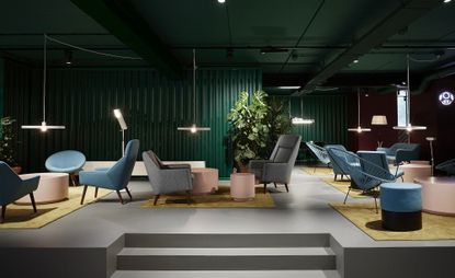 The Student Hotel lounge with grey floor, bottle green corrugated walls, blue, pink and grey armchairs, low hanging disk lamps