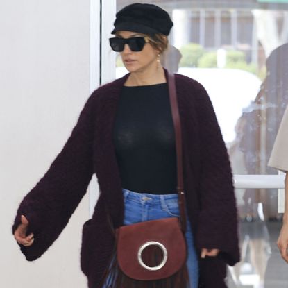 Jennifer Lopez wearing an oversize fringe sweater with a newsboy cap and flare jeans