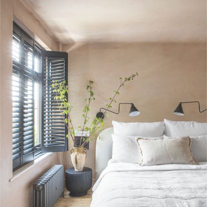 A neutral bedroom scheme with natural beddings, house plants and black shutters