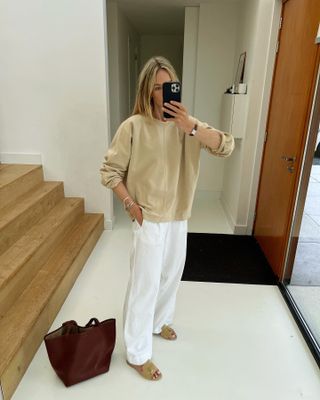 A woman wearing a tan sweater, white pants, tan slide sandals, and a Cartier Tank cocktail watch.