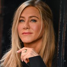 Jennifer Aniston has golden blonde hair and smiles while wearing a black long sleeve top