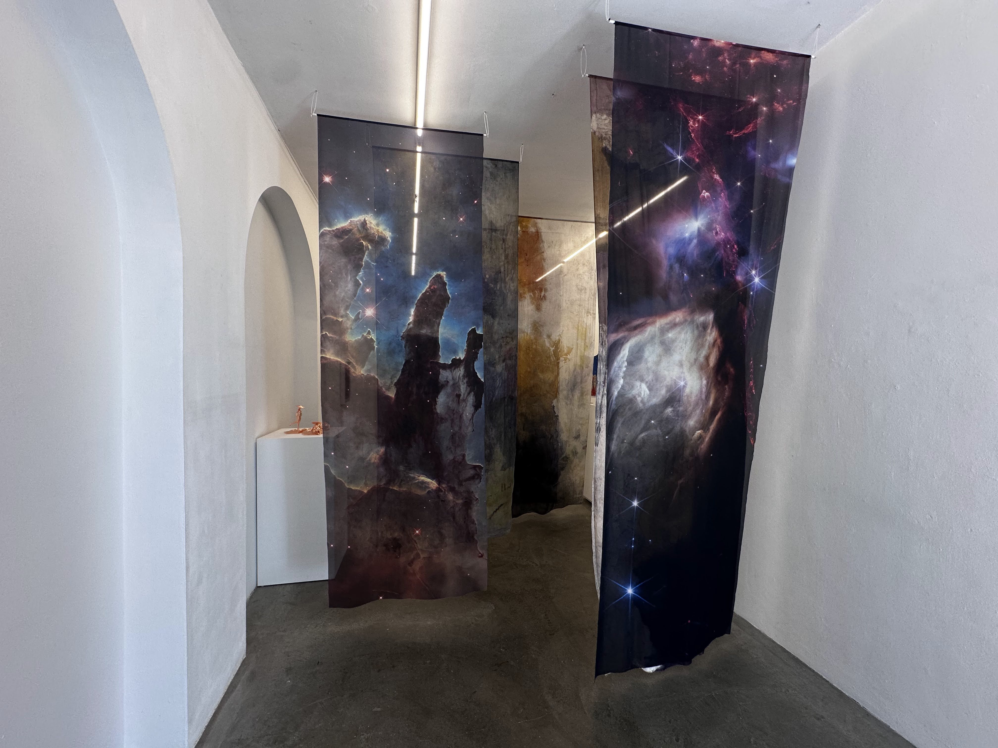 Cloth tapestries of images from the James Webb Space Telescope hang in a narrow white hallway. 