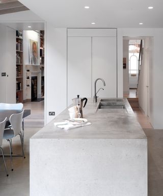 kitchen countertop trends, white modern kitchen with concrete island with sink, open plan dining/kitchen space, view to hallway and living room