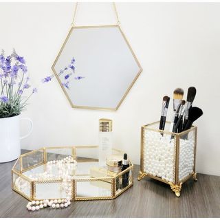 gold-edged trinket tray sits on a vanity with a pot of the same style and mirror nearby