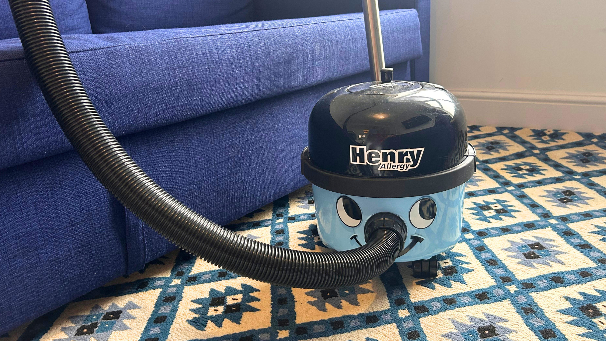 Megan's henry allergy vacuum cleaner on a blue patterned rug with a blue sofa in the background