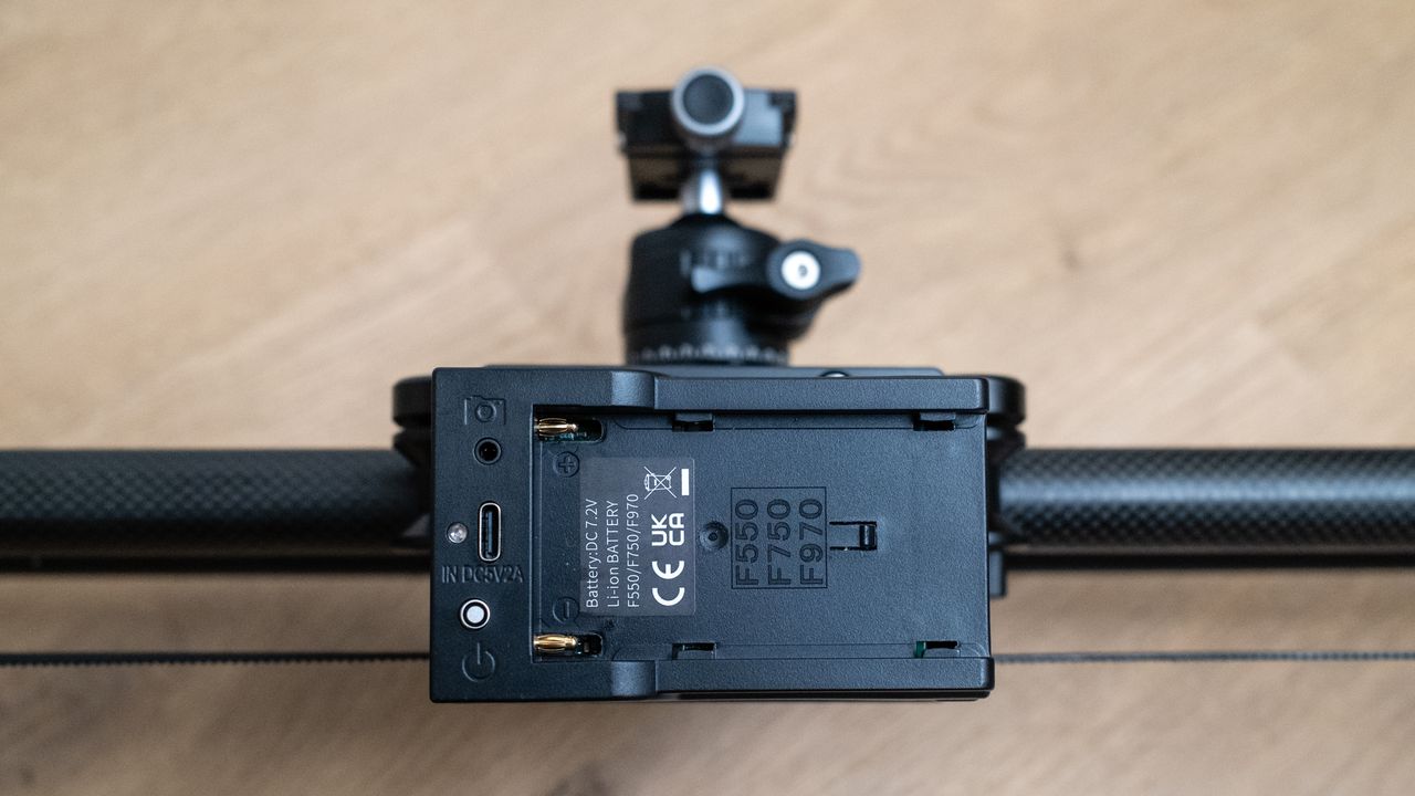 Close up of the battery connection on a Neewer ER1 Motorized Carbon Fiber Camera Slider on a wooden surface