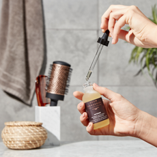 A person holding a dropper bottle of Grow Gorgeous serum in a bathroom. 