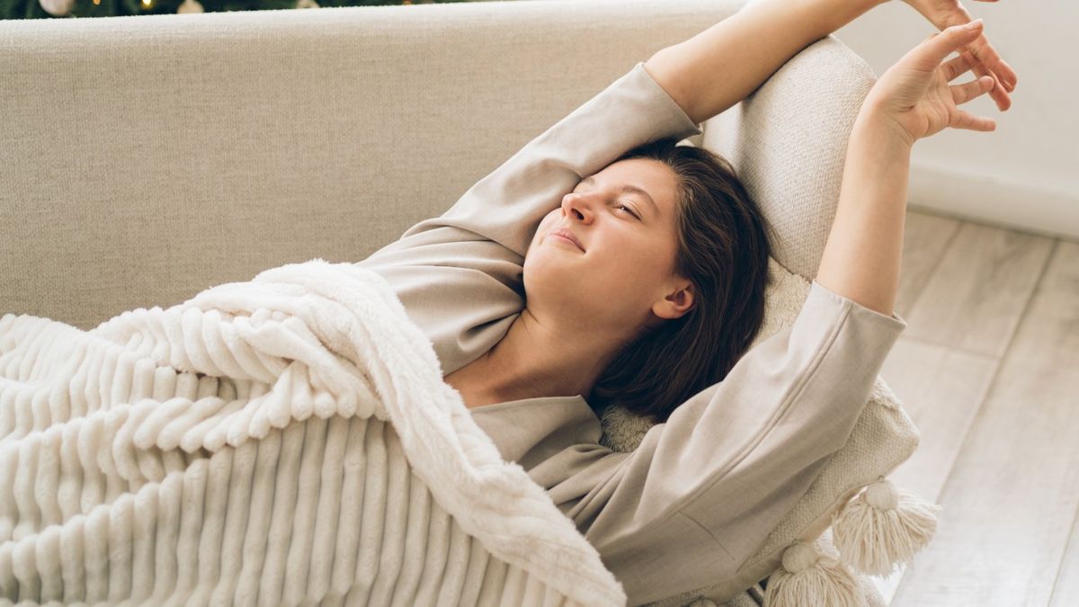 Woman taking a nap under a blanket on a sofa stretching