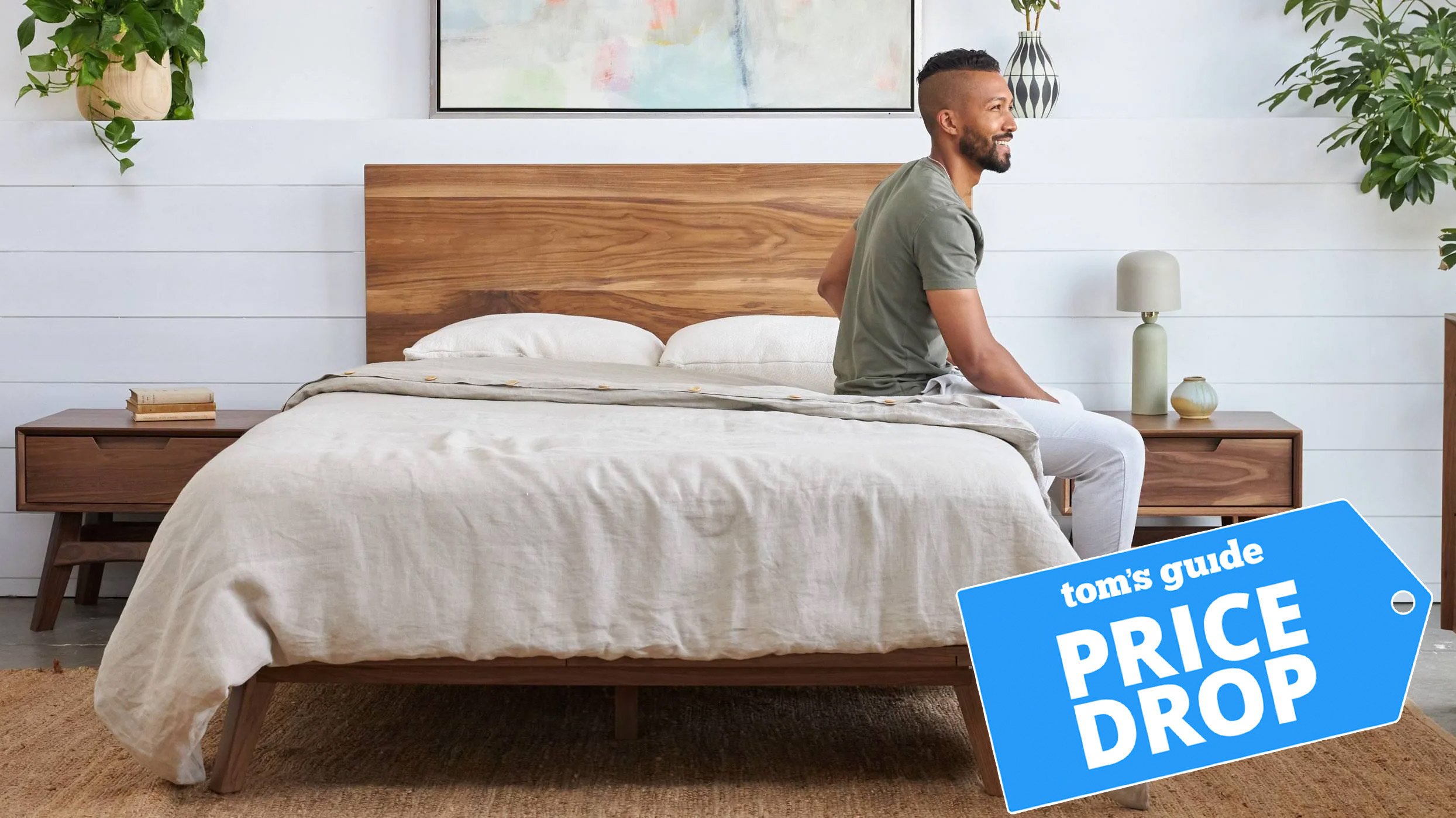 A man sits on the edge of an Avocado Green Mattress, with a Tom's Guide badge overlaid saying "PRICE DROP"