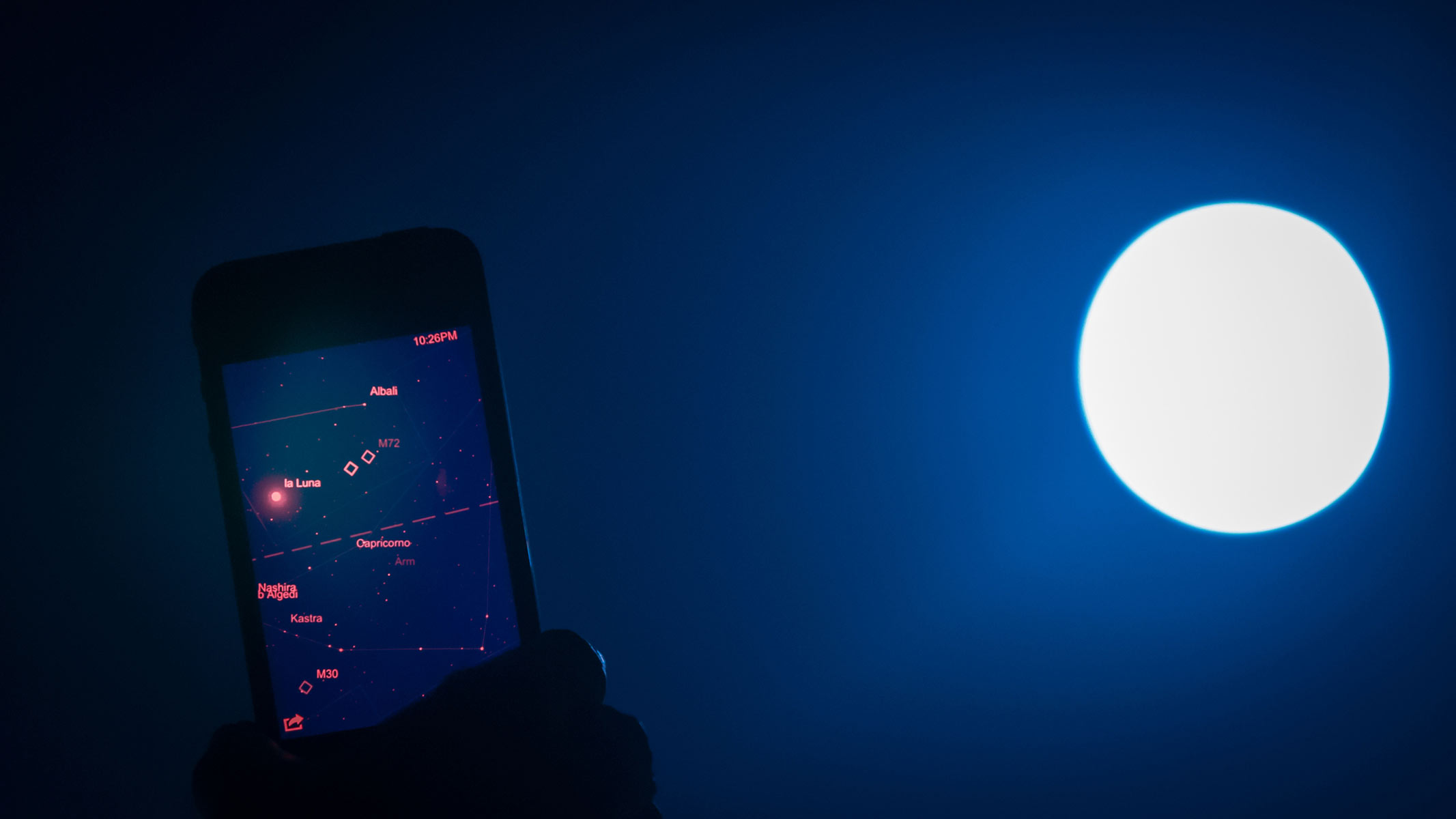 A smartphone with a red star diagram against a dark sky with a bright white moon on the right-hand side.