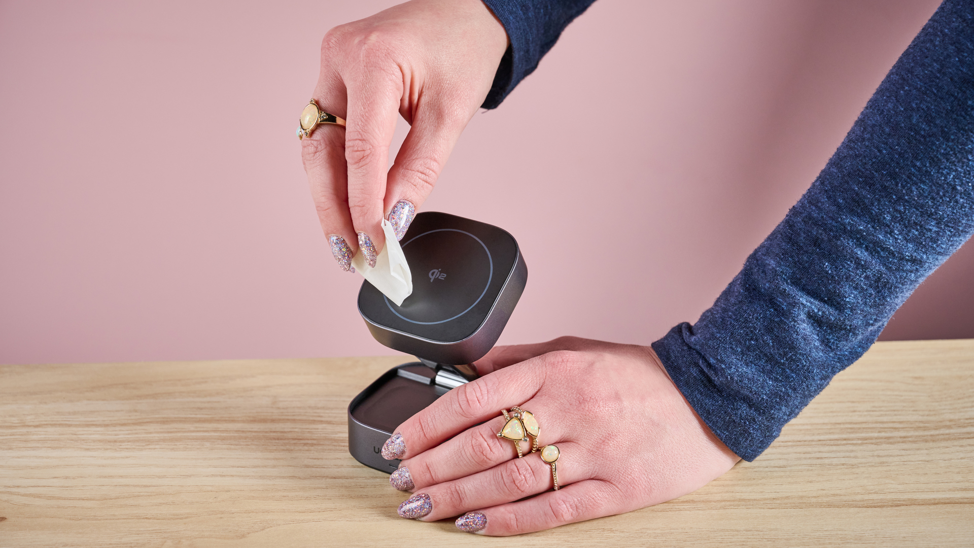 A woman is using an alcohol wipe to clean the surface of a wireless phone charger.
