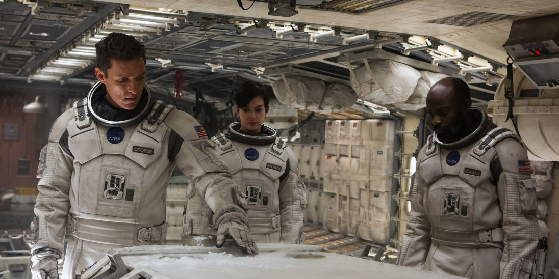 A still from the movie interstellar in which three cast members dressed in spacesuits are looking down at something inside a spaceship