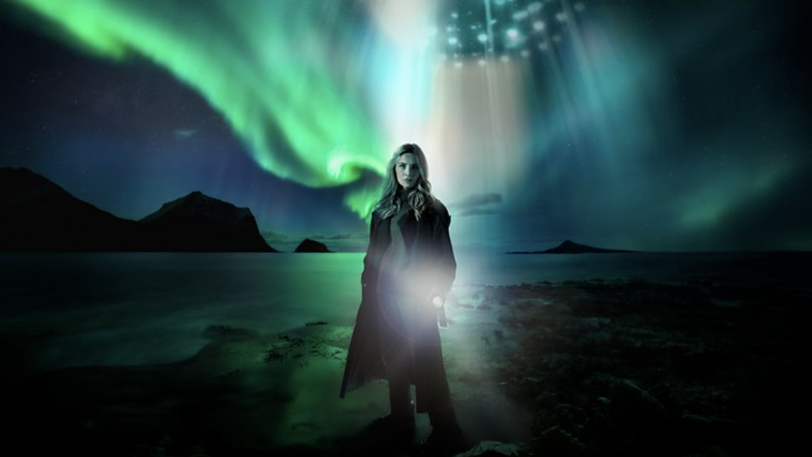 Sian Eleri standing in a coastal setting at night, with a UFO partly in view over her head in Paranormal: The Village That Saw Aliens