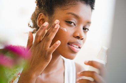 Woman applying cream to her face - best sun creams for dark skin
