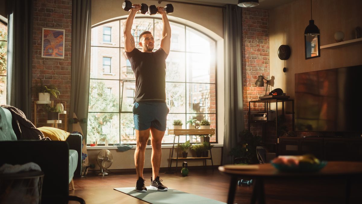 Man performing overhead press with dumbbells in living room