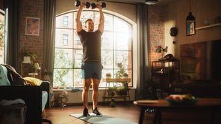 Man performing overhead press with dumbbells in living room