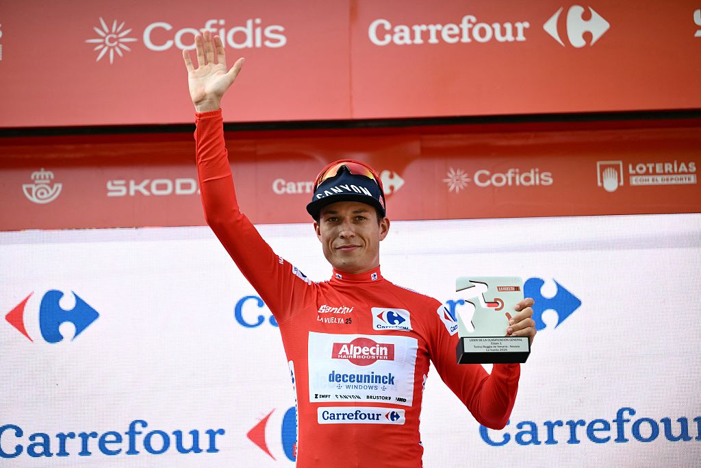 Team Alpecin's Belgian rider Jasper Philipsen wearing the red jersey celebrates on the podium of the first stage of the Vuelta a Espana, a 183 km race between Torino - Reggia di Venaria and Novara, in Italy's Piemonte region, on August 23, 2025. (Photo by Marco BERTORELLO / AFP)